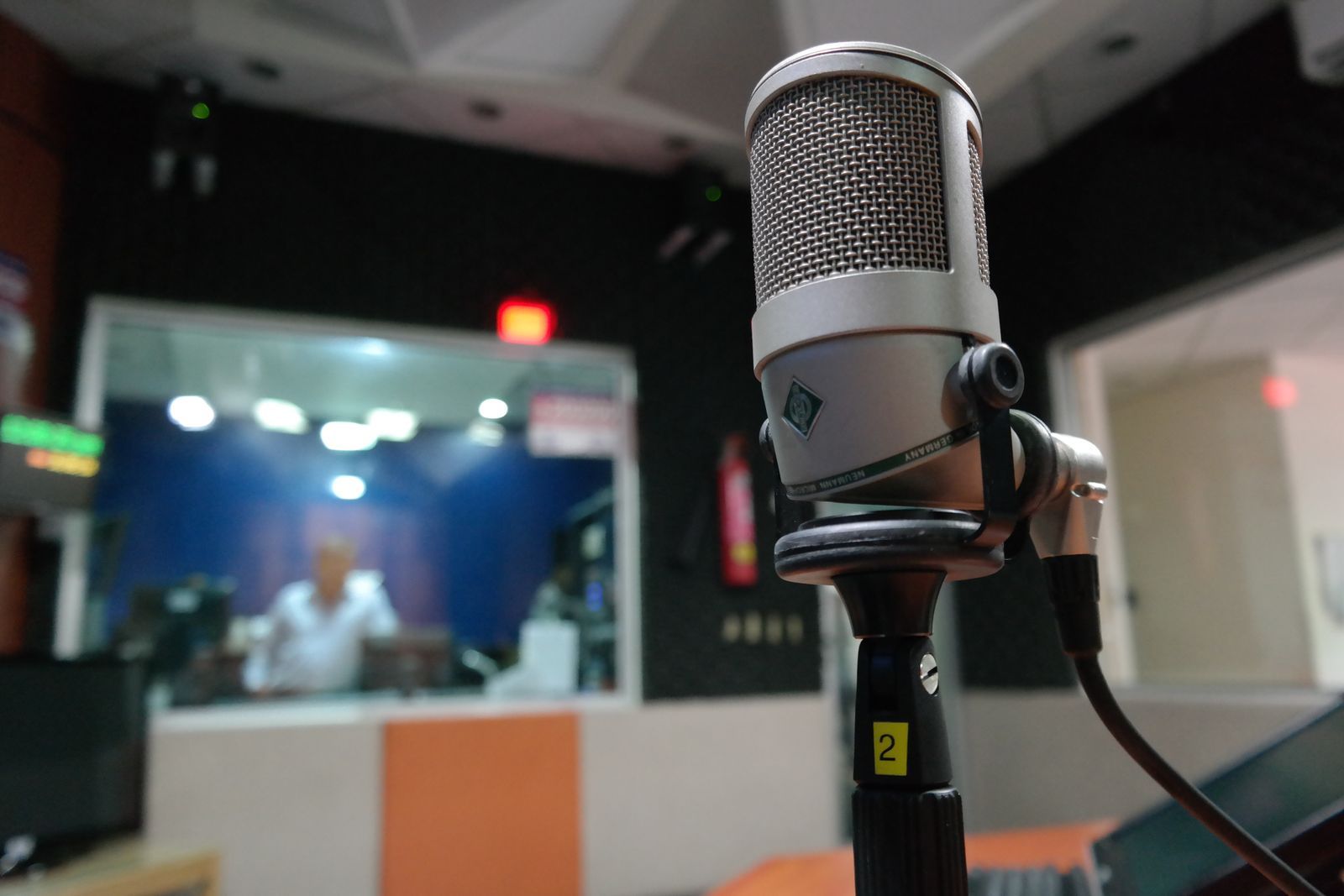 A microphone in a radio studio with the control room behind